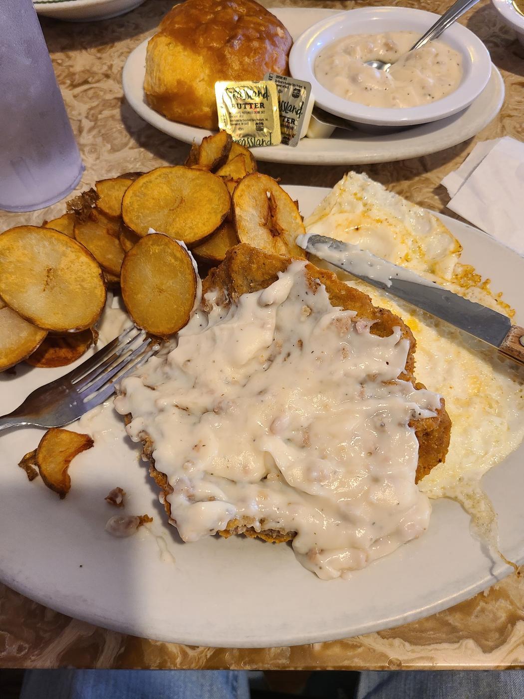 Country fried steak under gravy, with home fried potatoes, eggs and a biscuit